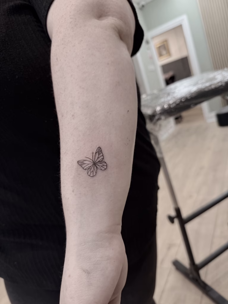Fineline butterfly tattoo on forearm – minimalist first tattoo at The Viper Pit Tattoo Studio in Manchester.
